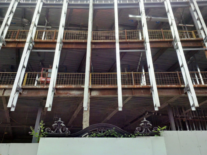 top of vintage law school gate peaks over construction wall on west side of new building