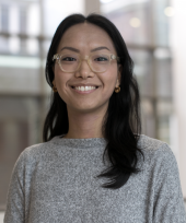 Yukiko, wearing a grey sweater, smiles in a photograph taken in the Jackman Law Building