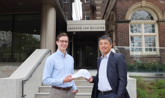 Law student D'Arcy White receives a law firm hat from alumnus Dr. Scott Guan in front of the doors to the Jackman Law Building 
