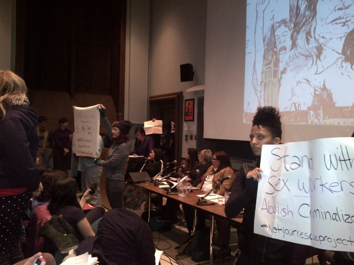 Protesters hold up signs in front of panelists